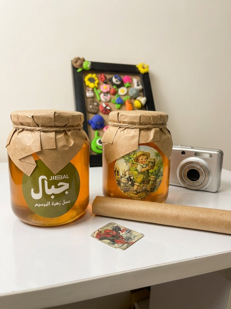 برطمانان من عسل زهور البرسيم من جِبال على طاولة بيضاء بجوار كاميرا ولوحة ملوّنة