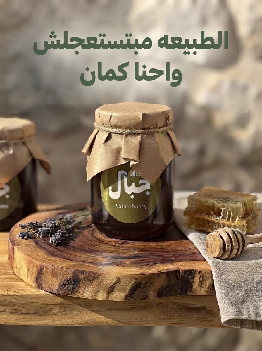 Jar of JIBAL black seed honey on a wooden slab beside honeycomb and a honey dipper, with the Arabic line "Nature takes its time, and so do we"