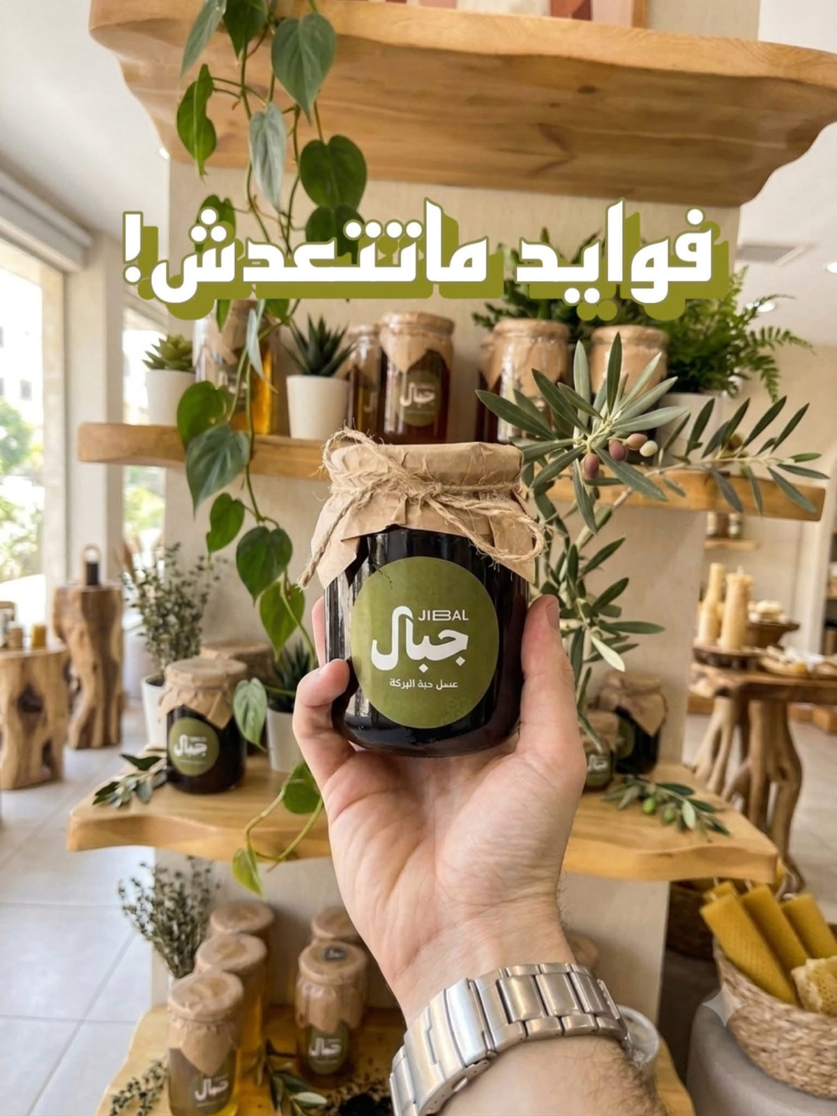 Hand holding a jar of JIBAL black seed honey in a shop with plants and shelves, with an Arabic slogan overlay